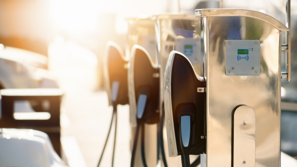 3/4 medium closeup of electric charging stations with cars parked in front. Sun flares give the whole image a warm feel.