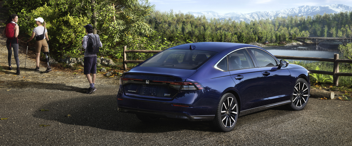 3/4 rear view of a parked blue Accord overseeing a forest and mountains. A hiker walking away from it.